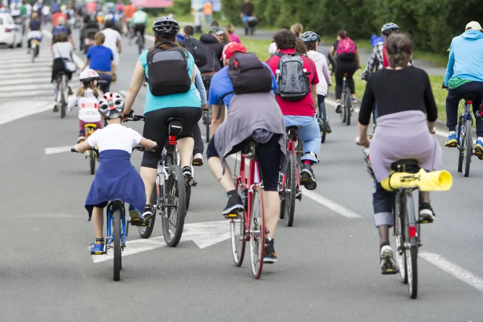 Large group of people and children on bikes in street.